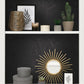 Decorative shelf with a gold mirror, plants, and framed artwork against a black textured wall.